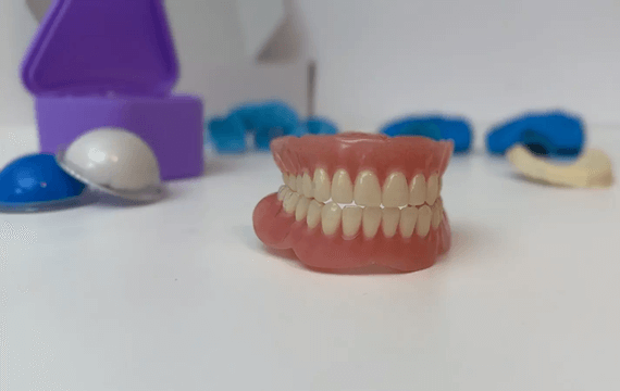 A model of a tooth alongside a toothbrush and denture reline kit, illustrating dental care and hygiene essentials.
