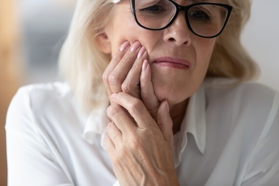 A woman holds her jaw in pain, indicating a toothache, while considering denture reline services for gum discomfort.